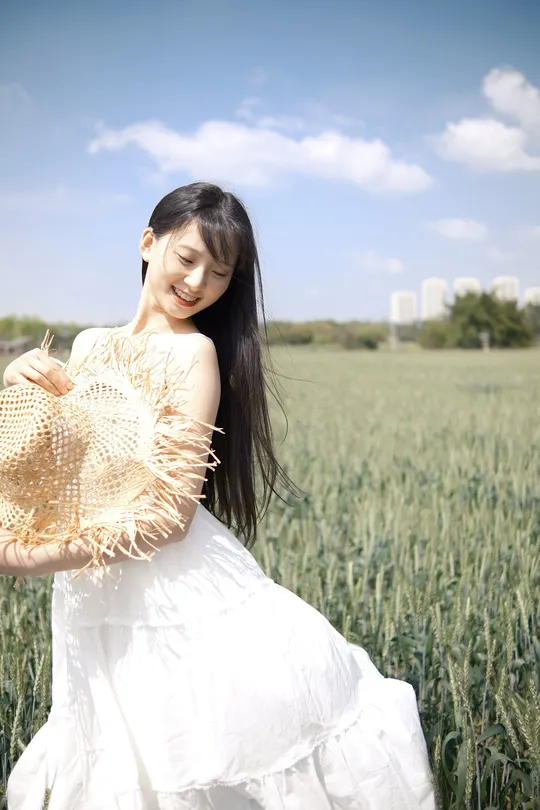 美丽的年轻女子穿着一件白色连衣裙 戴着帽子站在麦田里。