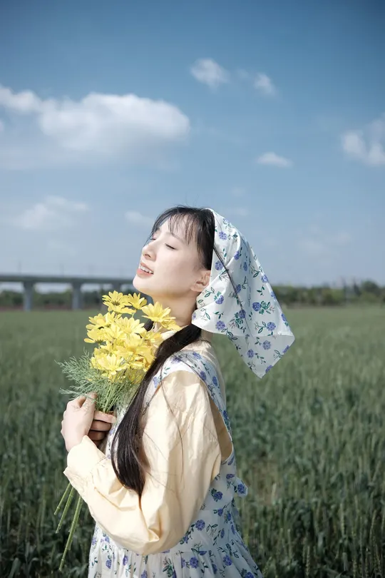一位穿着连衣裙的年轻女子在田野中拿着黄色花朵。