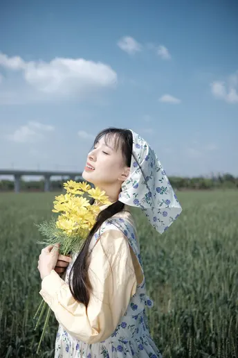一位穿着连衣裙的年轻女子在田野中拿着黄色花朵。