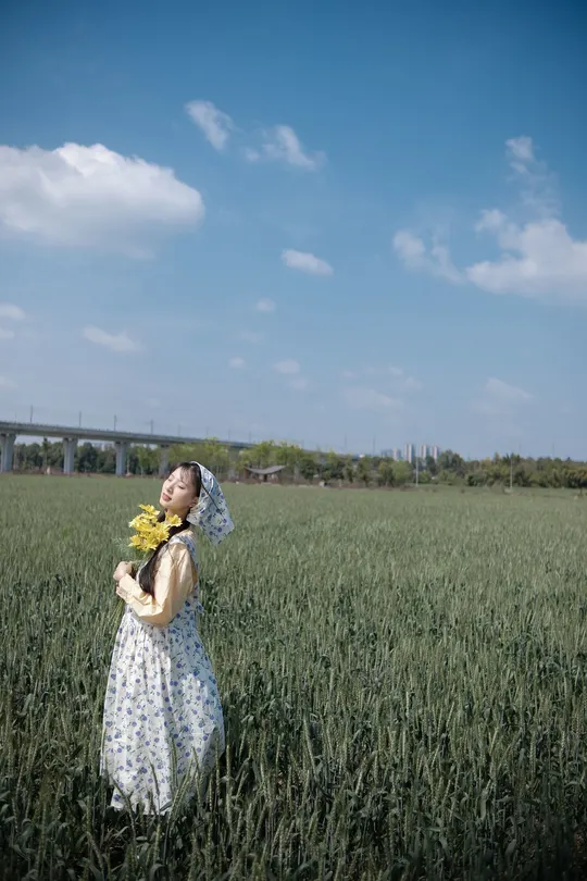 一位穿着连衣裙的年轻女子在绿色的田野中嗅着黄色的向日葵