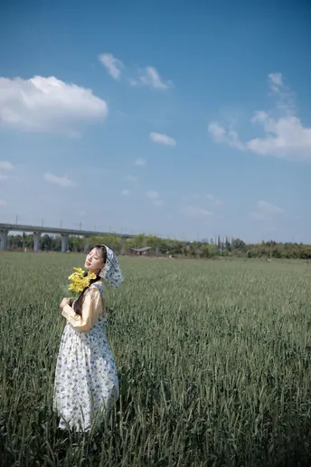 一位穿着连衣裙的年轻女子在绿色的田野中嗅着黄色的向日葵