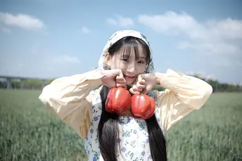 一位年轻女子手持红番茄站在田野中