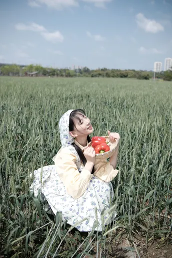 一个年轻女子坐在绿草地上 手里拿着一个装满红苹果的碗。