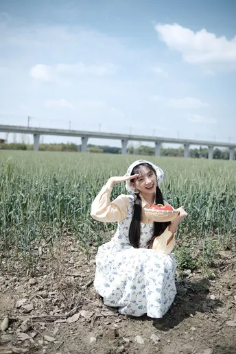 一个穿着连衣裙的年轻女子坐在田野里 手里拿着一盘食物。