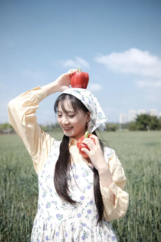 一位穿着连衣裙的年轻女子 头戴红苹果 戴着帽子站在田野中。