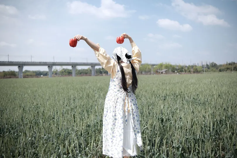 一位穿着连衣裙的年轻女子举着一个红苹果在头上