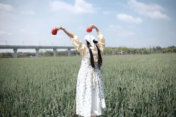 一位穿着连衣裙的年轻女子举着一个红苹果在头上