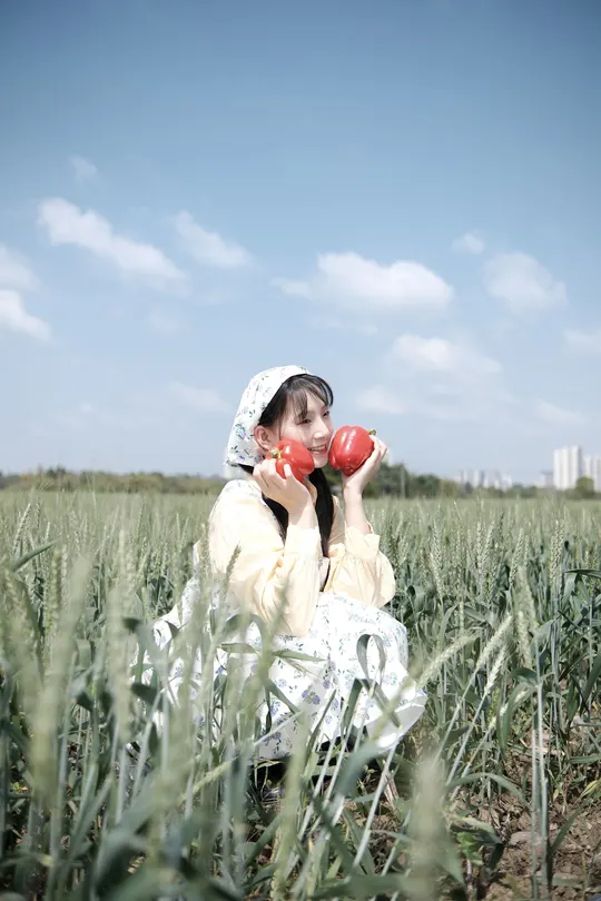 穿着裙子的一位女孩拿着一个红色的杯子坐在绿色的草地上