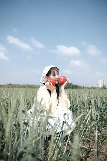 穿着裙子的一位女孩拿着一个红色的杯子坐在绿色的草地上