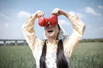 一位年轻女子举着一个红苹果在田野上