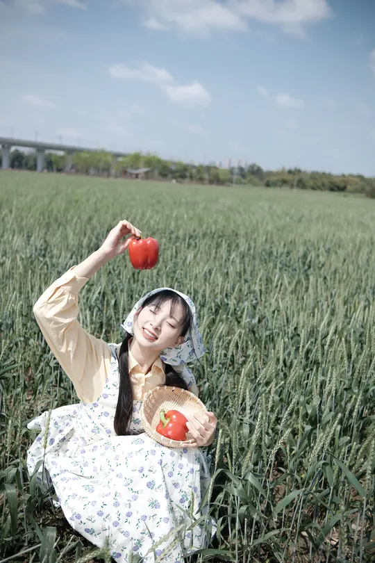 一位年轻女子坐在田野里 手里拿着一个红苹果。