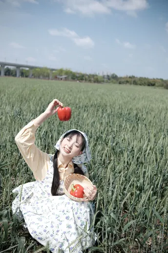 一位年轻女子坐在田野里 手里拿着一个红苹果。