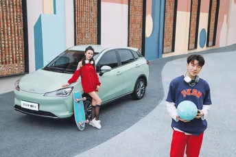 一个年轻男子拿着一个球站在一个年轻男孩的滑板旁边