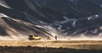 一辆黄色卡车穿越沙漠 背景是山脉 前景是车辆中的人。