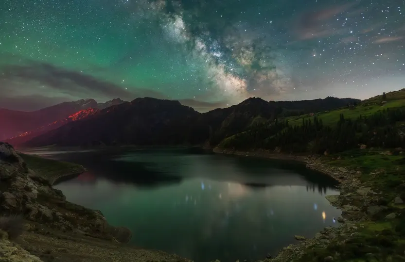 群山中的美丽夜晚 天空中繁星闪烁 前景中有一片湖泊。