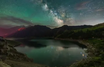 群山中的美丽夜晚 天空中繁星闪烁 前景中有一片湖泊。