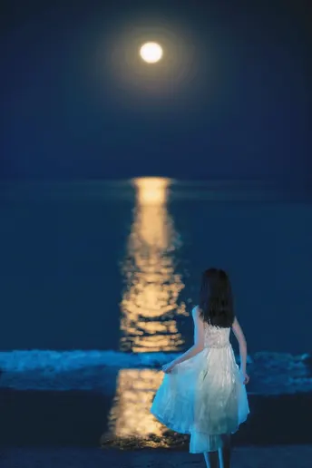 夜晚 一个穿着蓝色连衣裙的小女孩在海边 水面上挂着满月。