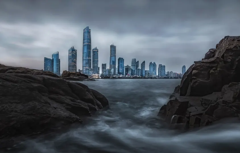 从海洋视角看城市及其摩天大楼 前景中有水域和岩石。