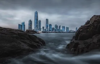 从海洋视角看城市及其摩天大楼 前景中有水域和岩石。