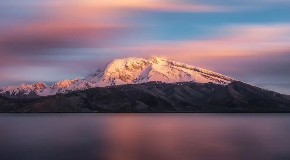 夕阳下 湖中倒映着一座被白雪覆盖的山 天空中是紫色的。