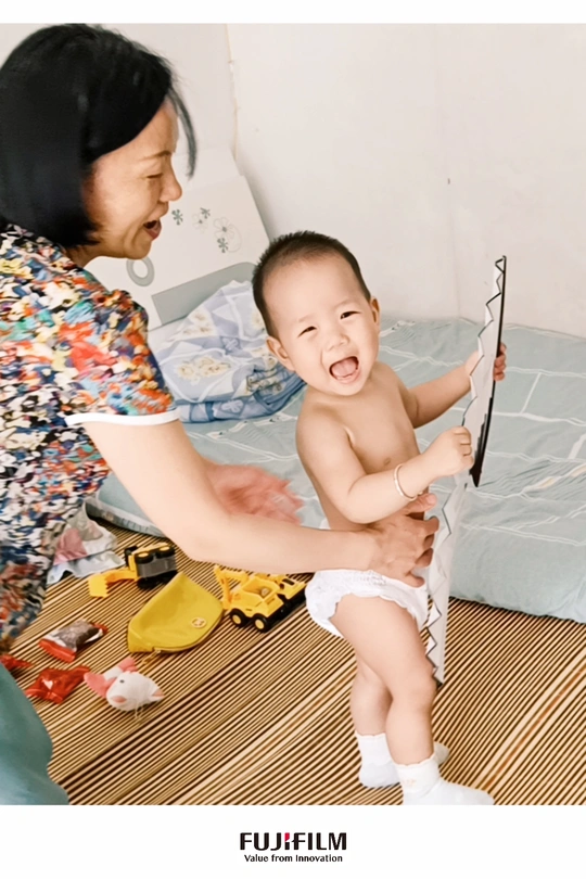 一位女士拿着雨伞对着地板上的一个小孩微笑