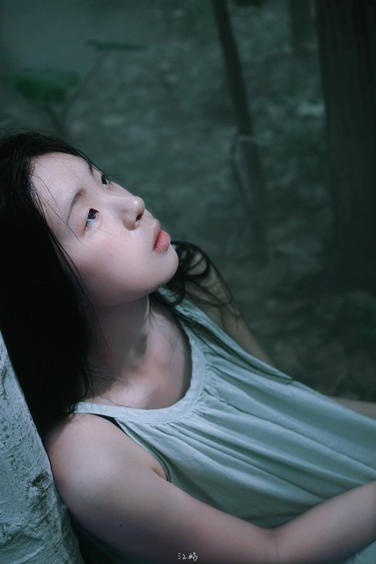 一位年轻女子穿着白色连衣裙坐在森林中的水边