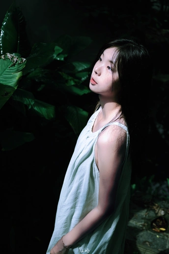 一位穿着白色连衣裙的年轻女子站在绿色雨伞下的人物肖像