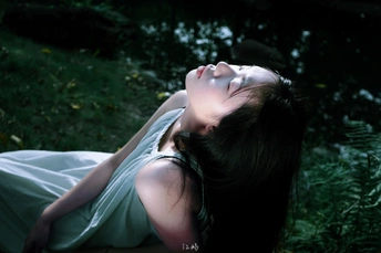 一个女孩穿着白色裙子躺在森林中的绿草地上