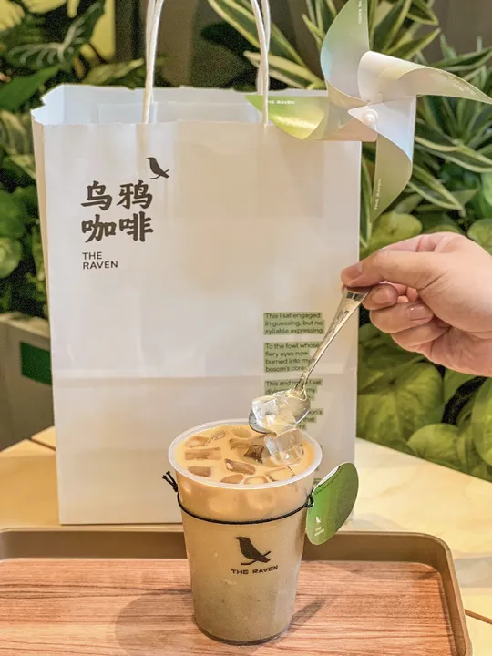 一个人在杯子旁边 手里拿着一根勺子 杯子里面装着咖啡 旁边还放着一个袋子。