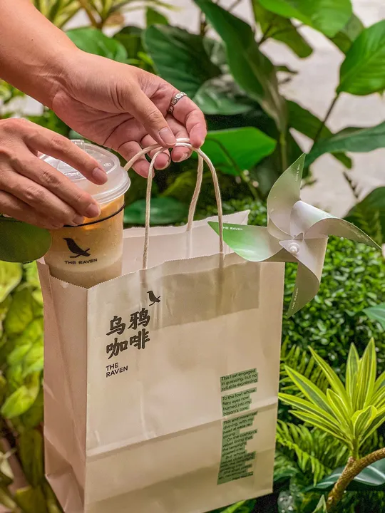 一个人在绿植前拿着一个塑料杯子喝咖啡