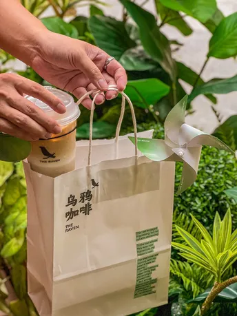 一个人在绿植前拿着一个塑料杯子喝咖啡