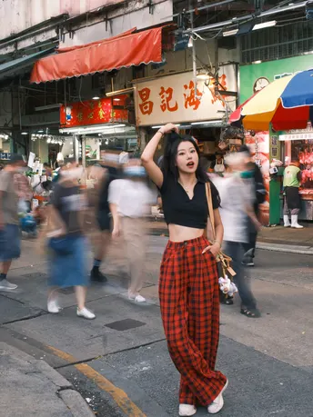 一位穿着格子裤子的年轻女子走在一条拥挤的街道上