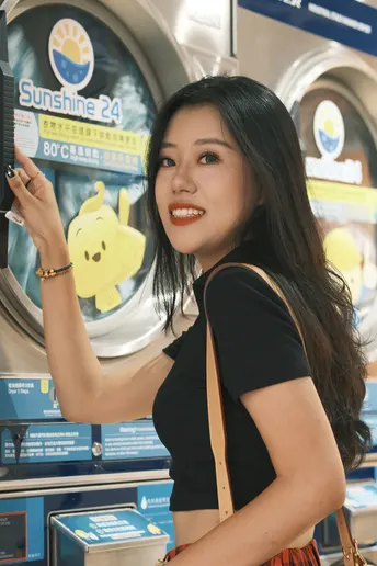 一位年轻女子手持相机站在硬币机前