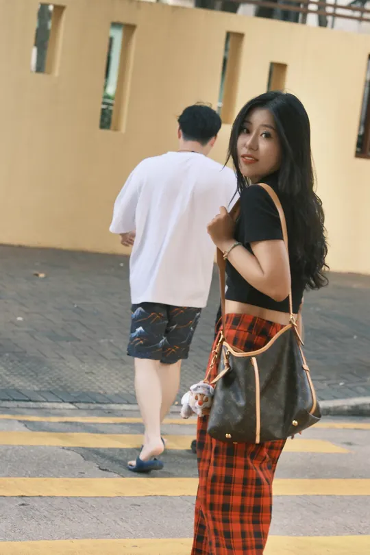 一位穿着格子裤子的年轻女子和一位穿着黑色裤子的年轻男子穿越人行横道。