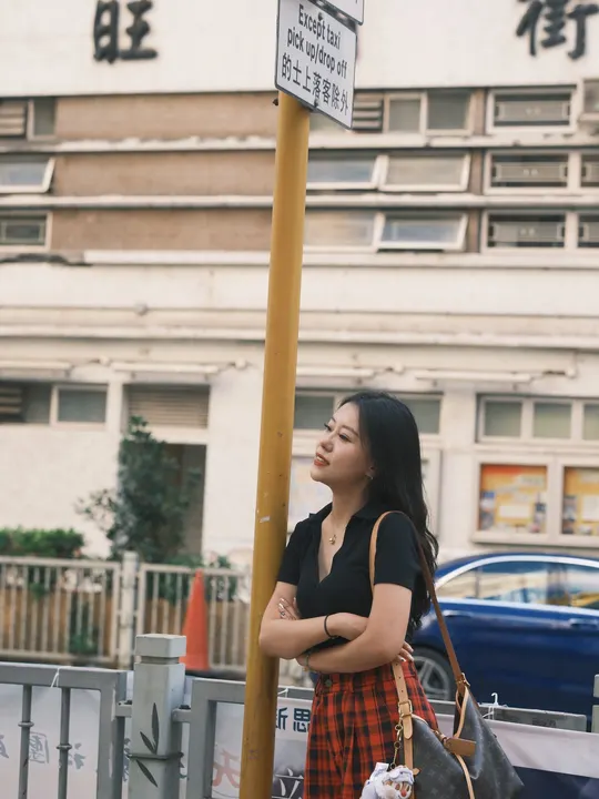 站在一栋建筑前 旁边有一根电线杆 电线杆上有街道标志 一个年轻女子拿着一个袋子。