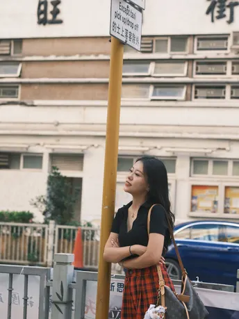 站在一栋建筑前 旁边有一根电线杆 电线杆上有街道标志 一个年轻女子拿着一个袋子。