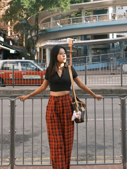 一位穿着红色格子裤子的年轻女子站在人行道上 手里拿着一把雨伞。