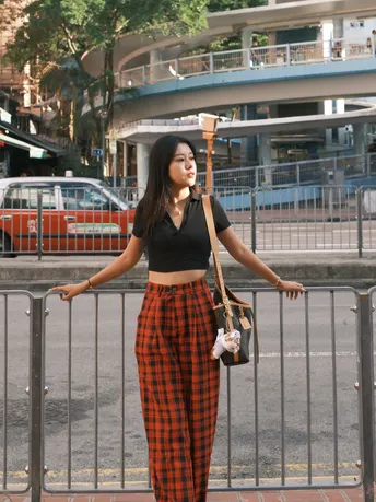 一位穿着红色格子裤子的年轻女子站在人行道上 手里拿着一把雨伞。