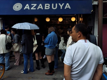 一个人站在商店前 周围有一群人经过 他手拿雨伞。