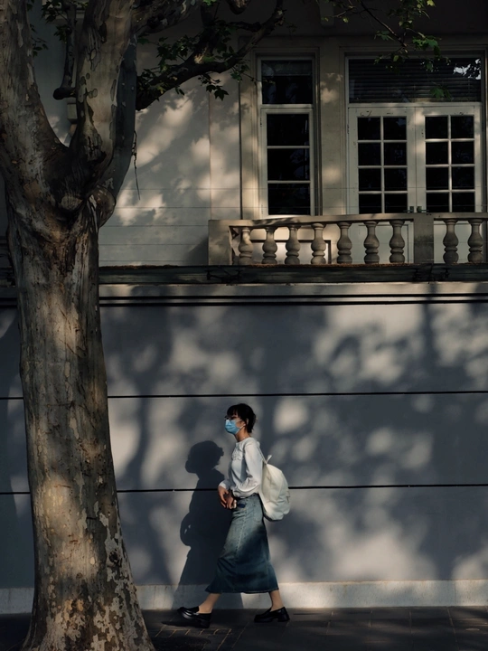 一个人戴着白色面具在人行道上走在白色建筑前 墙上有些阴影。