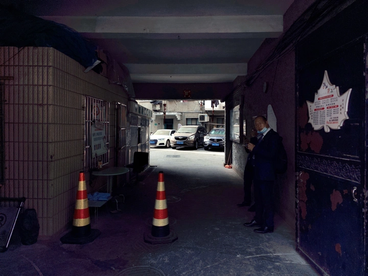 一个穿西装的男人站在一条黑暗的巷子里 旁边有一栋建筑。