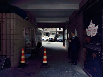 一个穿西装的男人站在一条黑暗的巷子里 旁边有一栋建筑。