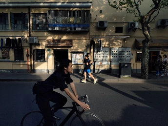 一位妇女骑自行车沿着一条街道 旁边有一位男子骑自行车。