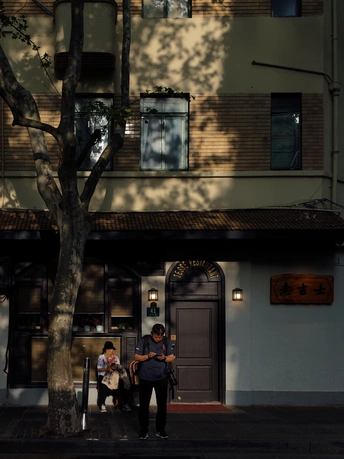 一条街道 一座建筑 一棵树 一把长凳 一位妇女站在人行道上 带着一个坐在地上的孩子。