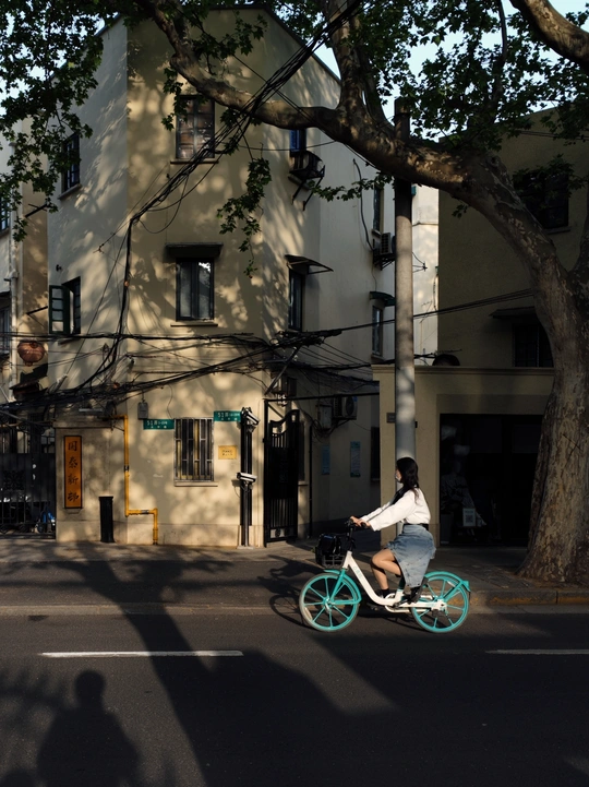 一位女士骑着一辆蓝色自行车沿着一座建筑旁的街道行驶。