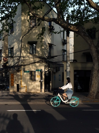 一位女士骑着一辆蓝色自行车沿着一座建筑旁的街道行驶。