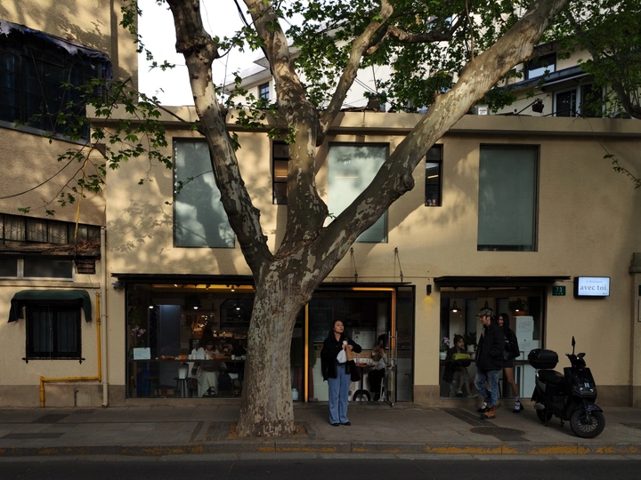 前方有一栋建筑 前方有一棵树 前方有一辆摩托车 前方有一名男子站在人行道上。