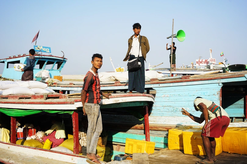 几个男人和一个年轻男孩站在靠近小船的水码头上。