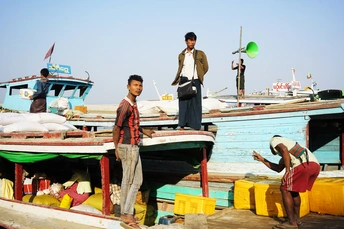 几个男人和一个年轻男孩站在靠近小船的水码头上。