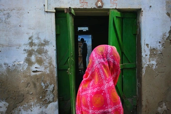 一位穿粉红色纱丽的女士站在一扇绿色门前